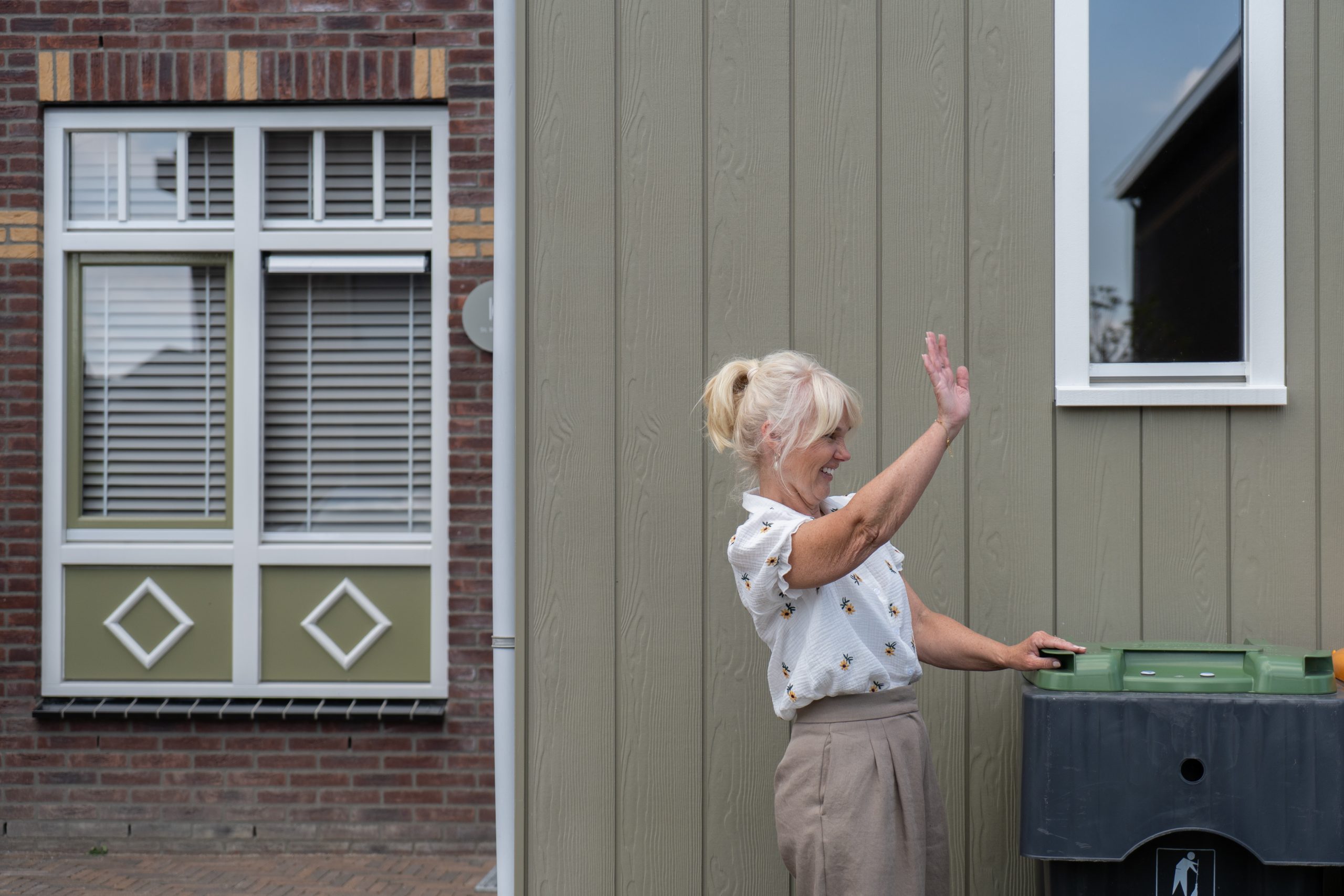 Vrouw staat voor woning en zwaait.