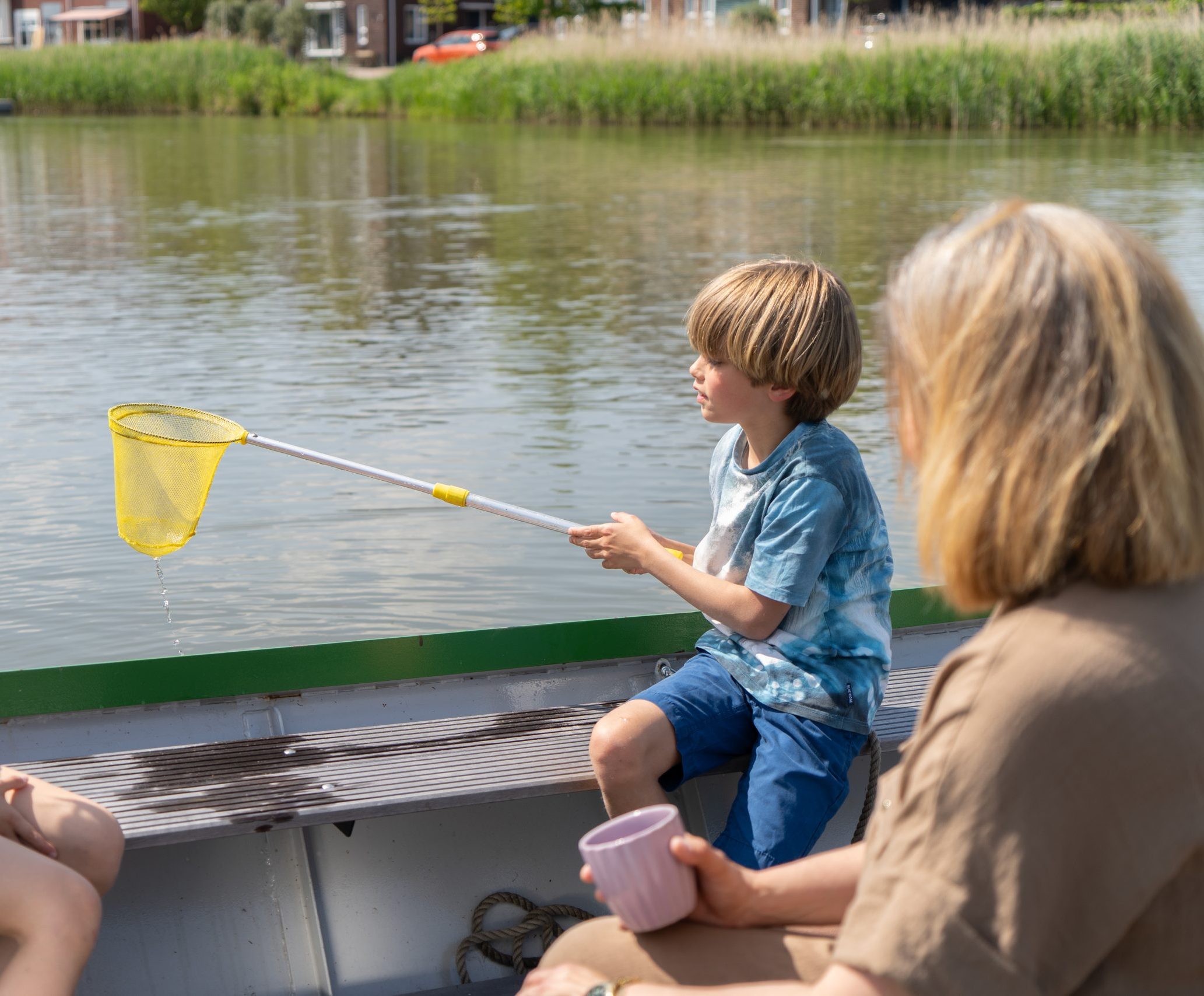 Gezin zit in een boot en de twee kinderen spelen met het water.